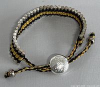 Full view of the bracelet showing the black and gold braided cord with silver beads and the round silver clasp.