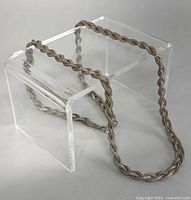 Full view of the twisted rope chain necklace displayed partly over a clear acrylic stand, showing the texture and length.