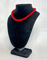Red coral bead necklace displayed on a black bust stand, showing the full length and uniform spherical shape of the beads.