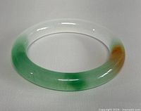 Front angle photo of the round jade bangle showing the green and brownish-orange coloration and smooth polished finish.