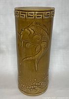 Front view of cylindrical stand showing embossed jumping koi fish and wave motif beneath Greek key border