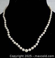 Front view of the 17-inch pearl necklace displayed on black velvet bust showing round white pearls and gold-filled clasp.