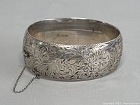 Photo of the wide sterling silver bangle bracelet showing the etched floral design and safety chain.