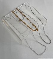 Photo of two necklaces displayed on a clear stand, one silver chain and one gold-filled chain.