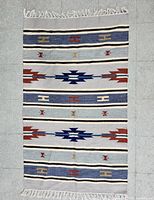 Top-down view of flatwoven kilim rug laid flat on floor, showing full geometric tribal pattern and fringed edges.