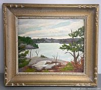 Full view of the framed landscape painting showing the gold-toned frame and the entire artwork featuring water, trees and rocks under a cloudy sky.