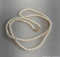 Full view of the pearl necklace laid out on a neutral background showing the length and strand of pearls.