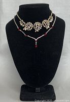 Full front view of vintage rhinestone necklace on black bust display, showing floral cluster design and red stone accents