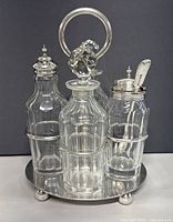 Front view of the cruet set on the silver plated tray with handle showing four glass bottles with detailed stoppers and lids