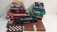Photo of assorted board games stacked including Yahtzee, Bingo, Rummikub, Pictionary, McDonald's Enigmate, and various puzzles.