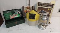 Photo showing entire lot including metal tackle box with fishing accessories, Flow Troll bait bucket, portable gas stove in box, fish grilling basket and metal lantern.