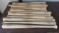 Photo of 12 wooden baseball bats lying side by side showing their full length and markings.