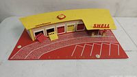 Front and top view of the Shell model railroad service station building showing the yellow roof with Shell logo, curved parking lot and four garage doors.