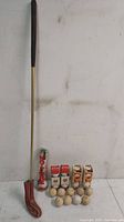 Full view of vintage wood-shafted golf putter with leather headcover and assortment of vintage golf balls, including new old stock and used balls, plus sealed Nicklaus Golden Bear ball tube.