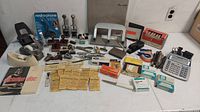 Wide shot showing an assortment of vintage office supplies on a white table including hole punchers, stamps, staplers, ink pads, and a calculator.