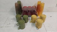Assortment of vintage plastic mugs and glasses in various colors including olive green, yellow, amber, and red, displayed on a white surface.
