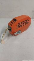 Side view of orange vintage Take-A-Tab ticket dispenser with ticket pulled out with visible numbers