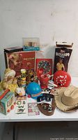 Photo showing assorted vintage toys arranged on table including Fisher Price Music Box TV, red rotary phone toy, toy clock, animal figurines, sunglasses, small collectible cards, and a straw hat.