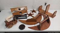 Full view of wooden decor items and shelves on white table including heart-cut corner shelf, wooden stars, crescent moon shelf, curved piece with dowels, broken wagon model, and small wooden items.