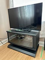 40-inch Insignia flat-screen TV on a black stand with curtains in the background. TV screen is off and remote is on the stand below the screen.