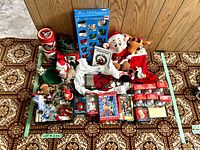 Photo showing assorted Christmas ornaments, including Simpsons characters, Rudolph waterballs, and glass ornaments, plus several Christmas-themed tins and plush figurines on a patterned carpet.