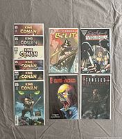 Nine comic books arranged in three columns on a gray surface, varying in titles, artwork, and colors. Protective sleeves visible.