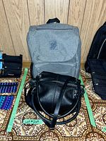 Black Danier leather purse and grey Home Depot branded knapsack placed on patterned fabric background against wood panel wall.