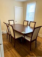 Full view of dining table with 6 chairs arranged around it, showcasing cherry wood finish and cream fabric upholstery.