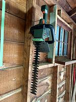 Black & Decker electric hedge trimmer hanging on a wooden wall, showing full length and blade detail with serrated edges.