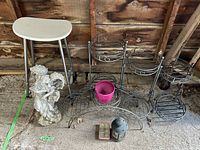 Full lot photo showing all items together in garage setting including stool, two plant stands, pink planter pot, angel garden statue, tea light candle holder and candles.