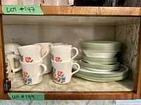 Photo showing stacked Corelle dish set items including plates, bowls, and cups with a tulip floral pattern and green trim inside a wooden cabinet shelf.