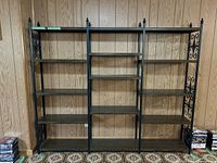 Front view of vintage metal bookshelf with three sections and dark wood shelves against wood-paneled wall.