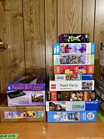 Overall lot showing puzzle roll away box, several jigsaw puzzles with various piece counts and brands including Ravensburger and LEGO sets stacked on a wooden surface.