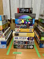 Stack of nine assorted puzzles from various brands with visible puzzle box artwork including Nuance, Hidden Shapes, Kitchen Essentials, Springbok, Eurographics, and others.
