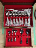 Entire silverware set including 8 forks and 8 spoons in wooden box with red lining, some pieces sealed in plastic bags