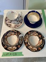 Four teacups and saucers displayed from above showing detailed floral and color patterns and overall condition.