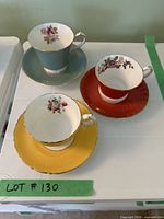 Top view of three teacups with corresponding saucers showing floral decorations and distinct colors (teal, yellow, red).