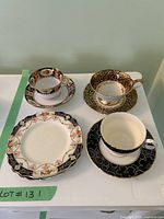 Front view of three ornate teacups with matching saucers and two small plates showing detailed patterns and colors.