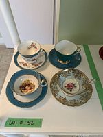 Top view of all four teacups and saucers showing floral and gold designs on teal and white china.