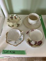 Top view of four teacups with matching saucers from different fine china brands showing patterns and colors.