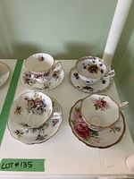 Top view photo showing all four teacups and saucers arranged on a white surface with clear floral patterns and gold trims