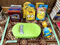 All DVD boxed sets for Seasons 1-5 with colorful spine designs plus character-shaped special head edition cases for Seasons 6-12 with various Simpsons character faces shown, Mighty Beanz green case, and Bart Simpson piggy bank