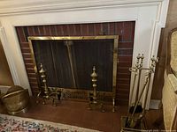Wide angle photo showing brass fireplace tools, screen, and bucket arranged near fireplace