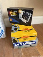 Stack of boxed camera equipment including Kodak Disc 4000 camera outfit, Kodak Prestape Universal Splicer boxes, Olympus Infinity Mini Dlx camera