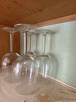 Two tall stemmed wine glasses inverted on a shelf with dusty wooden back and light green painted surface.