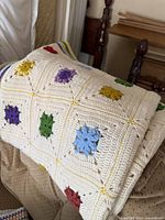 Photo of folded granny square afghan showing multicolor crocheted floral squares on cream background draped over a chair.