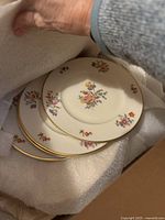 Four stacked floral china dinner plates with multicolor flowers and gold trim on edge, wrapped in foam.