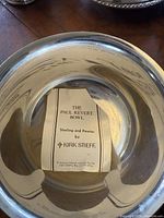 Close-up of large sterling and pewter bowl labeled as 'The Paul Revere Bowl' by Kirk Stieff with maker's label inside.