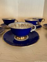 Several deep blue teacups with gold accents on bases and handles, placed on matching deep blue saucers with gold rim.