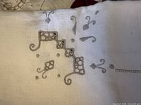 Close up of embroidered linen fabric with geometric and floral cutwork designs in neutral tones